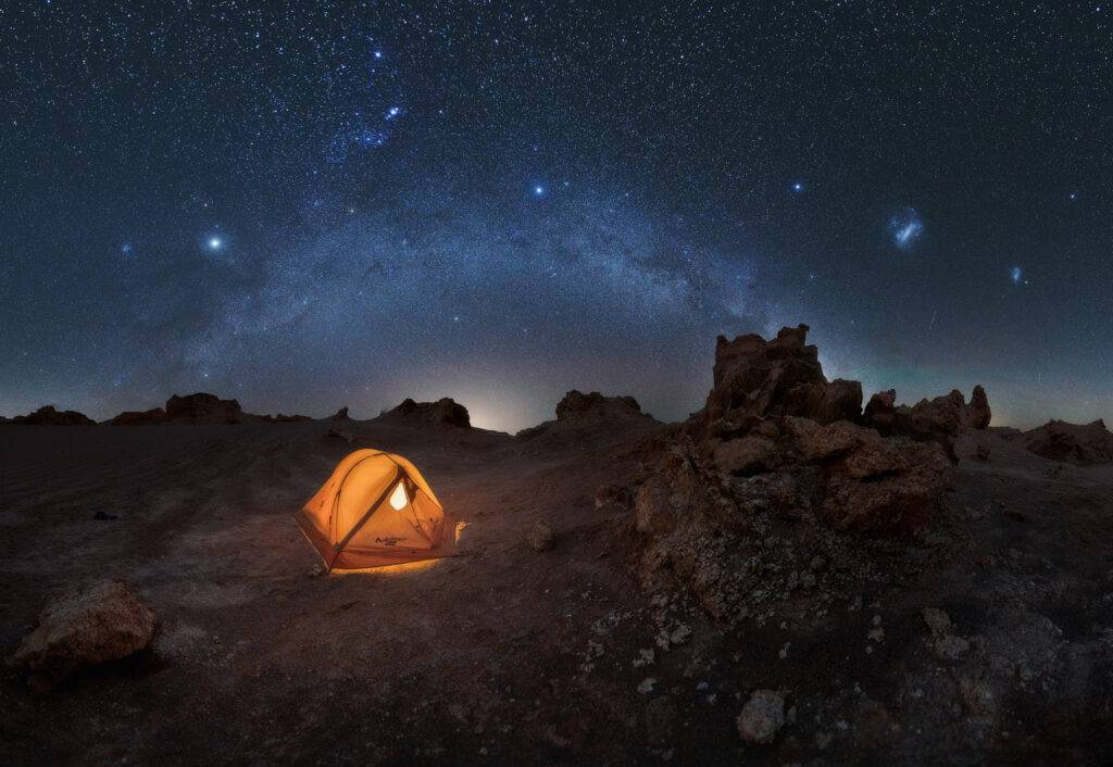 Fotografía tomada en el desierto de Atacama, mostrando el brazo de Orión sobre una carpa en medio del paisaje árido. Ideal para transmitir la experiencia de acampar bajo las estrellas.