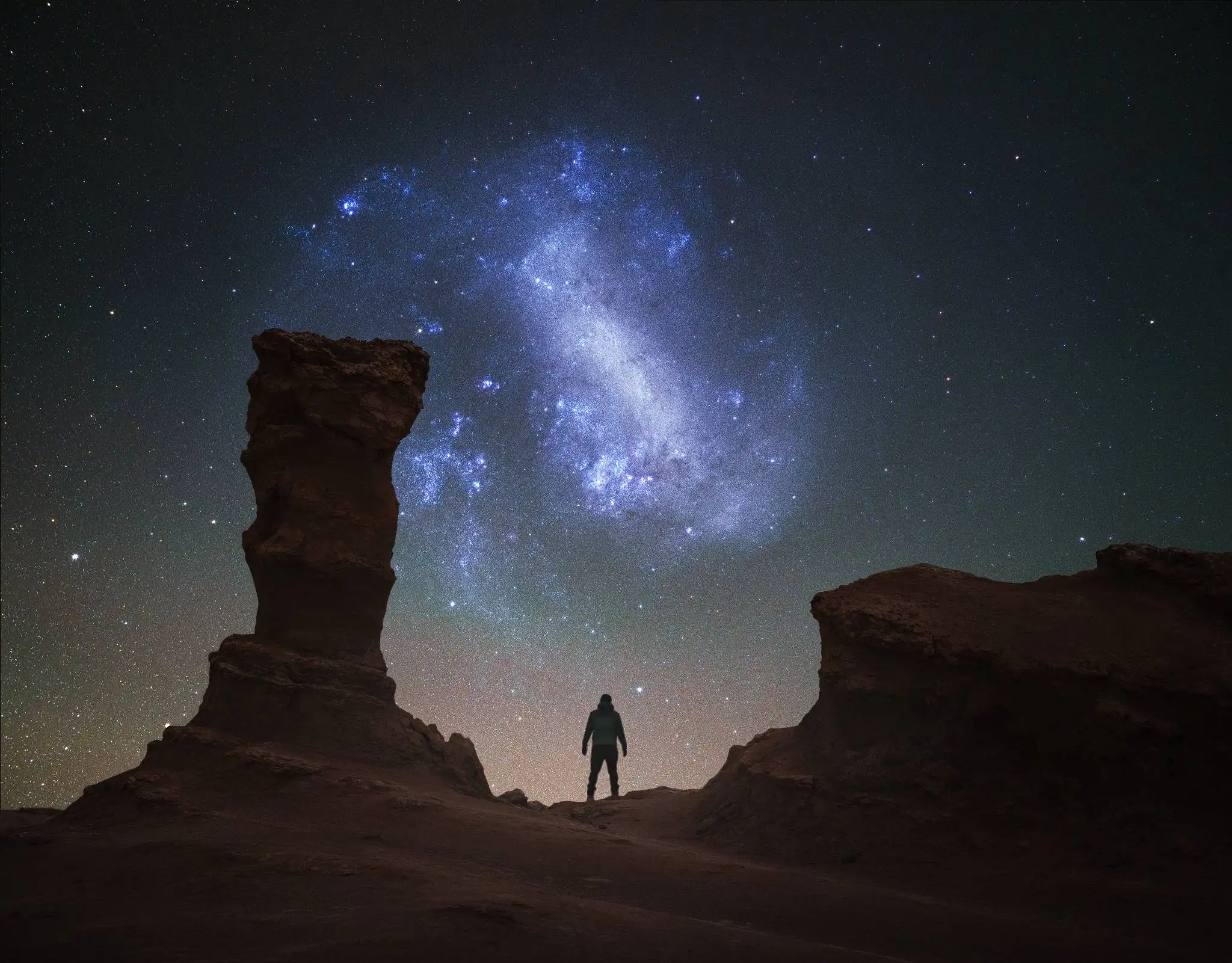Silueta de fotógrafo contemplando la Gran Nube de Magallanes sobre las formaciones rocosas del desierto de Atacama, galaxia satélite de la Vía Láctea visible a ojo desnudo desde el hemisferio sur