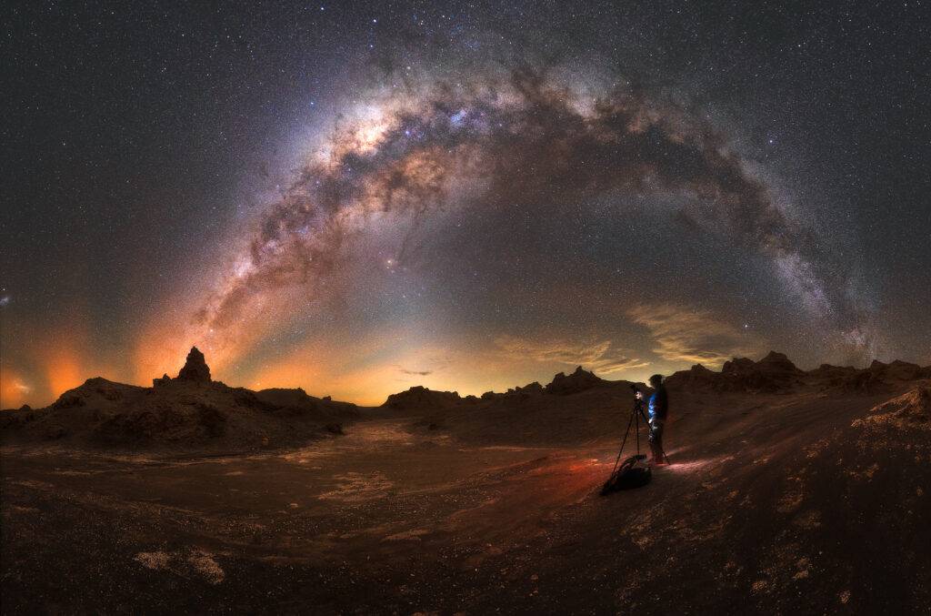 Fotógrafo capturando el arco completo de la Vía Láctea sobre formaciones rocosas del desierto de Atacama, Chile