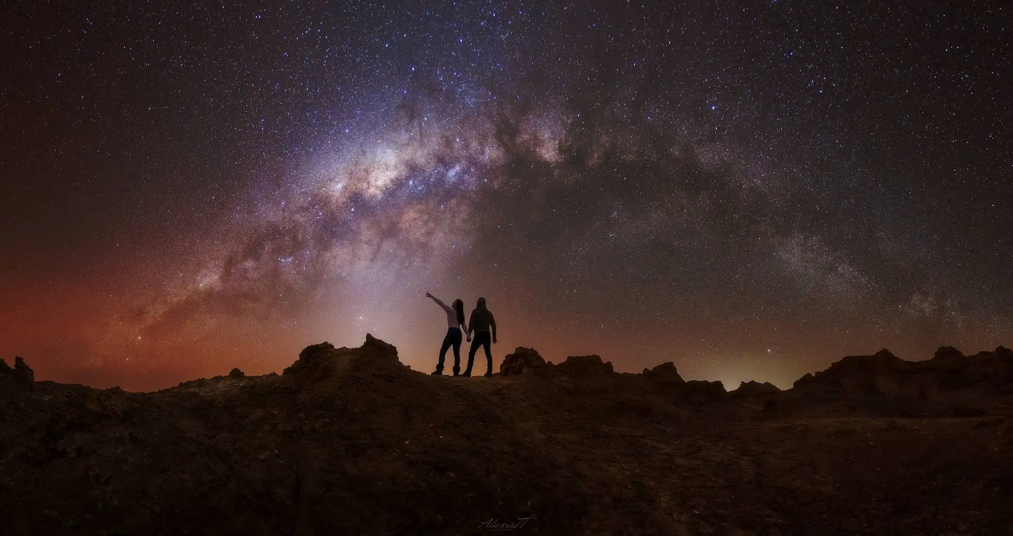 Pareja contemplando el arco de la Vía Láctea desplazándose hacia el oeste sobre las formaciones rocosas del desierto de Atacama, septiembre-octubre, San Pedro de Atacama
